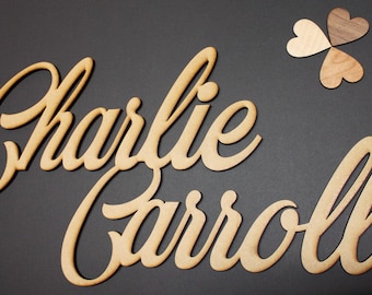 May include: Wooden cutouts of the names "Charlie Carroll" in a cursive font, with a trio of wooden heart shapes. The names are in a light brown color, set against a dark gray background. The hearts are in shades of brown.