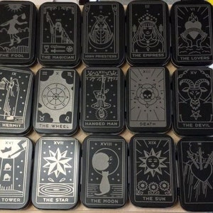 May include: A set of 22 tarot cards in black and silver with a silver metallic finish. The cards are arranged in two rows of 11 cards. Each card features a different tarot symbol and name. The cards are in a vintage style.