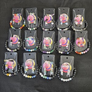 May include: Fourteen sets of jewelry, each featuring a beaded bracelet and matching earrings displayed on a black card. The bracelets are made of various colorful gemstone beads, including lava rock, while the earrings feature dangling chip beads.