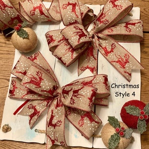 May include: Christmas Style 4. Decorative Christmas bows with a reindeer pattern in red and white on a burlap ribbon. The bows are arranged on a white wooden background with decorative burlap spheres and holly accents.