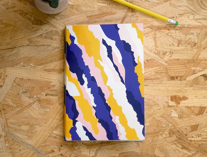 May include: A notebook with a colorful abstract design featuring yellow, blue, pink, and white stripes. The notebook cover has a textured, wavy pattern.