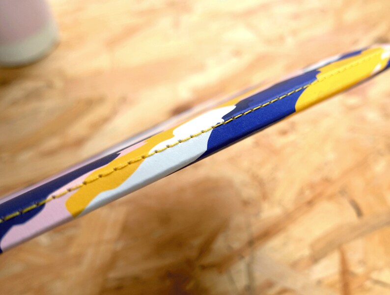 May include: Close-up of a blue, yellow, and pink patterned strap with yellow stitching. The strap is made of a soft, flexible material.
