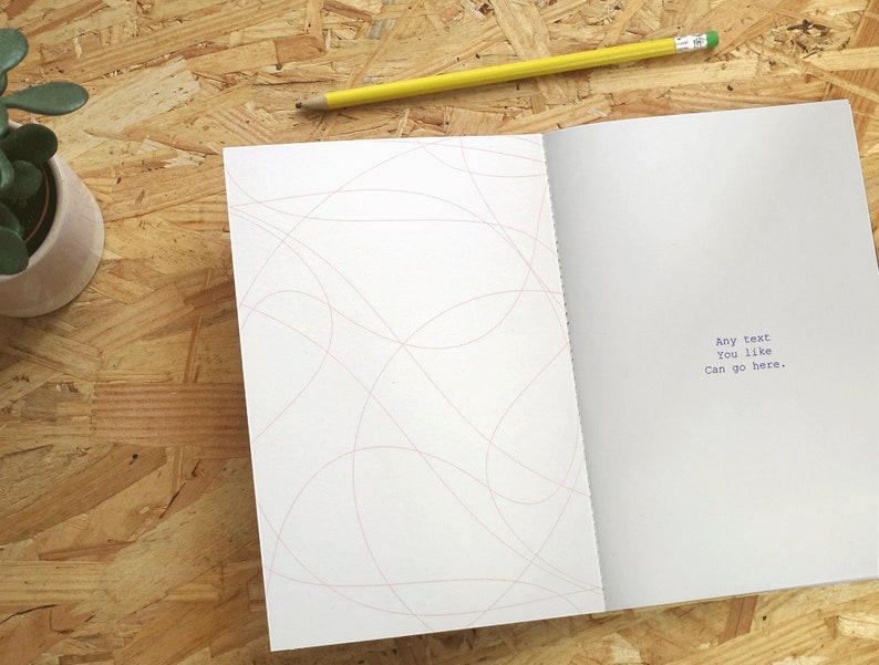 May include: An open notebook with a white cover and pink lines on the left page. The right page has the text "Any text you like can go here." printed in blue.