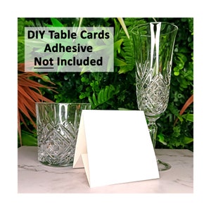 May include: White blank table cards with a folded design, sitting on a white surface next to a clear glass. The text "DIY Table Cards Adhesive Not Included" is visible in the background.