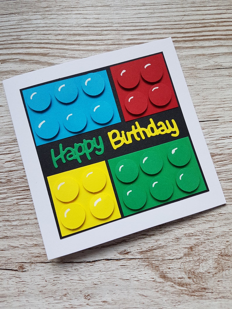 May include: A handmade birthday card featuring a colourful Lego block design with the words "Happy Birthday" in yellow lettering.