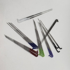 May include: A selection of silver bicycle spokes with coloured heads. The heads are painted in various colours, including red, blue, green, and purple. The spokes are arranged on a white background.