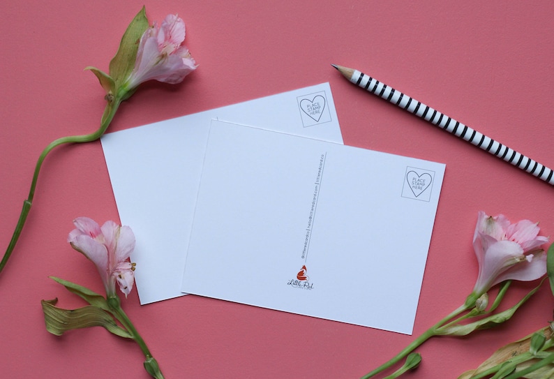 May include: Two blank white postcards with a red fox illustration and the text "Little Fox" on the bottom right corner. The postcards have a heart-shaped stamp with the text "Place Stamp Here" on the top left corner. The postcards are on a pink surface with pink flowers.
