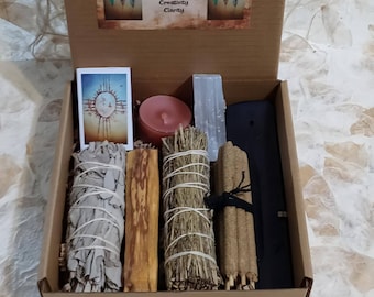 May include: A Native Dreams Smudge Set in a cardboard box. The set includes sage bundles, palo santo, a candle, incense, a selenite wand, and a card. The box has text that reads "Renewal, Energetic Clearing, Meditation, Divine Guidance, Peace, Creativity, Clarity."