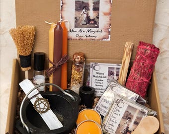 May include: A cardboard box containing a Witches Starter & Basics Set. Items include a small broom, three taper candles, a glass vial with dried herbs, a black cauldron with a pentacle charm, two orange tea lights, a wooden spoon, and sage.
