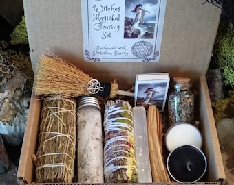 May include: A cardboard box labeled "Witches Magickal Clearing Set" contains a small broom, bundles of herbs, a jar of salt, a selenite wand, incense sticks, a matchbox, a small jar, and two candles. The box is decorated with a picture of a woman.