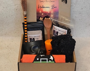 May include: A cardboard box filled with Halloween-themed items. Includes a small broom, a wooden spoon, a black mask, a candle, a pair of black socks, and a folded orange towel with a witch hat design. The box has a label that reads "Halloween Box."