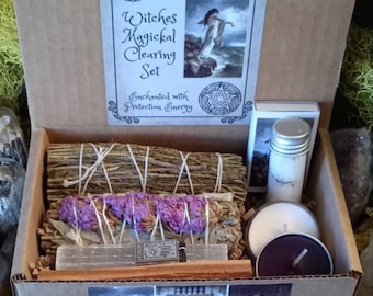 May include: A cardboard box labeled "Witches Magical Clearing Set" contains various items for spiritual practices. The box includes bundles of dried herbs, a small jar, candles, and a selenite wand. The set is designed for protection and energy clearing.