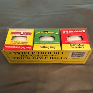 May include: A yellow box with three golf balls inside. The golf balls are labeled "Cloud-Flite Exploder", "Unputtaballo", and "Jetstreamer". The box says "The Triple Trouble The World's Best Trick Golf Balls".