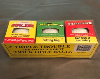 May include: A yellow box with three golf balls inside. The golf balls are labeled "Cloud-Flite Exploder", "Unputtaballo", and "Jetstreamer". The box says "The Triple Trouble The World's Best Trick Golf Balls".