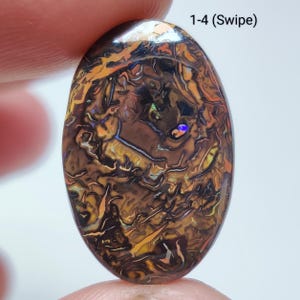 Puede incluir: Una piedra preciosa ovalada con un patrón complejo de remolinos marrones, naranjas y negros. La piedra tiene destellos iridiscentes de azul y amarillo. El texto "1-4 (Swipe)" es visible en la esquina superior derecha.
