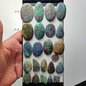 Könnte beinhalten: Eine Sammlung polierter Rubin-Zoisit-Edelsteine in verschiedenen Formen, darunter Ovale und Tropfen. Die Steine zeigen eine Mischung aus grünen, rosa und violetten Farbtönen. Eine Münze ist zum Größenvergleich enthalten. Die Zahlen 1-4, 5-8, 9-12, 13-17 und 18-22 sind links geschrieben.