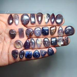 May include: A collection of polished gemstones in various shapes and colors, including teardrop, oval, and rectangular forms. The stones range in color from deep purple to clear with inclusions. The image includes the numbers 1-8, 7-16, 17-24, and 25-30.