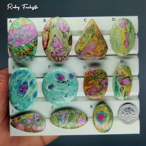 Pode incluir: Uma coleção de pedras preciosas polidas de Ruby Fuchsite em várias formas, incluindo ovais e em forma de gota. As pedras exibem uma mistura de cores, com inclusões de rubi rosa em fundos verdes, azuis e amarelos. O texto "Ruby Fuchsite" é visível.