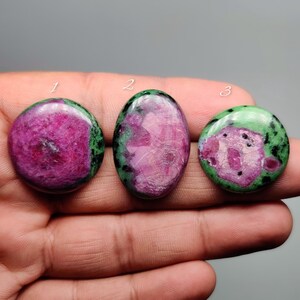 May include: Three polished ruby zoisite cabochons labeled 1, 2, and 3. The stones feature vibrant magenta and pink centers surrounded by mottled green and black mineral inclusions. Each piece has a smooth, rounded surface with a glossy finish.