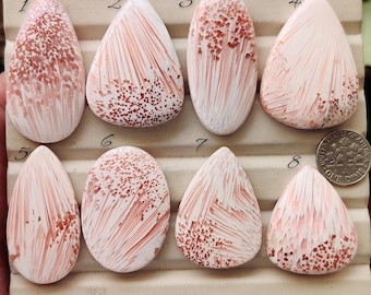 May include: Eight polished cabochon gemstones arranged on a display tray, numbered one through eight. Each stone features a white and pink radial pattern with small square-like inclusions. A US dime is placed next to stone eight for scale.
