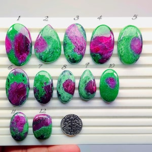 Può includere: Una collezione di dodici pietre preziose lucidate di rubino in zoisite, ognuna con un motivo unico di tonalità verdi e magenta. Le pietre preziose variano per forma e dimensione, con una moneta per la scala.