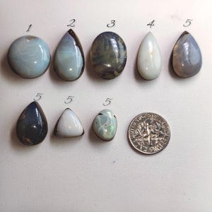 May include: A collection of polished gemstones in various shapes and colors, including blue, white, and gray. A U.S. dime is included for size comparison. The gemstones are numbered 1 through 5.
