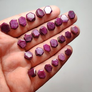 May include: A collection of small, hexagonal, deep pink to red gemstones arranged in rows. Each stone features a flat, polished top surface with distinct geometric edges, showcasing a consistent saturated color and a semi-opaque, natural texture.