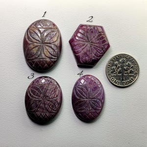 May include: Four carved gemstone cabochons in shades of purple and brown, with intricate floral and geometric designs. One is a hexagon, and the others are oval. A US dime is included for size reference.