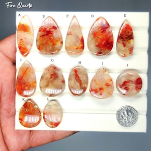 Puede incluir: Una colección de piedras preciosas de cuarzo de fuego en varias formas, incluyendo lágrimas, óvalos y formas puntiagudas. Las piedras muestran una mezcla de tonos claros, naranjas y rojos. El texto "Fire Quartz" es visible en la parte superior.