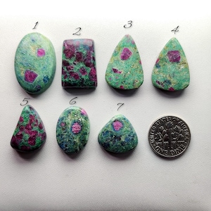 May include: Seven polished gemstones with a dime for size comparison. The gemstones are a mix of shapes, including oval, rectangular, and triangular. They feature a green matrix with red and pink inclusions, creating a unique pattern.