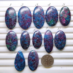 May include: Twelve polished gemstones, mostly oval, displaying blue, purple, and green colours. A U.S. dime is included for size comparison. The stones have a speckled appearance, with varying patterns and colour distribution.