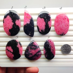 Puede incluir: Siete piedras preciosas de rodonita pulidas en varias formas, incluyendo ovaladas y de lágrima. Las piedras presentan un llamativo contraste de patrones rosas y negros. Se incluye una moneda como referencia de tamaño.