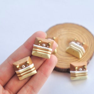 May include: Four brown and white keycaps with a cute bear face design. The keycaps are made of resin and have a glossy finish.