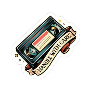 May include: A sticker featuring a retro VHS tape design in teal, black, and red. The tape is labeled with a cream-colored banner that reads "HANDLE WITH CARE" in black lettering. The design includes star accents.