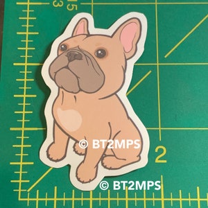 May include: A sticker of a cartoon French bulldog sitting with its tongue out. The dog is light brown with a pink nose and ears. The sticker has the text "BT2MPS" on it.