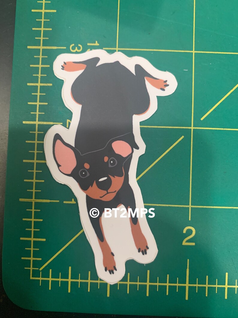 Puede incluir: Una pegatina de perro de dibujos animados negro y marr&oacute;n con orejas rosas. El perro est&aacute; boca abajo y tiene un fondo blanco. La pegatina tiene el texto "&copy;BT2MPS".