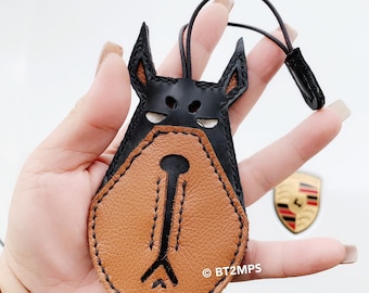 May include: A brown and black leather keychain shaped like a dog's head. The dog has a black nose and black eyes. The keychain has a black leather strap with a black leather loop at the end. The text "©BT2MPS" is visible on the keychain.