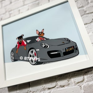 Op de afbeelding: Een ingelijste illustratie van twee honden die in een grijze Porsche rijden. De honden dragen rode en zwarte kleding. De auto heeft een kentekenplaat met de tekst "BT2MPS".