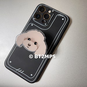 May include: Black phone case with a white border and a small white sticker of a dog's face. The case has a camera lens cutout with four gold rings around it. The text "&copy; BT2MPS" is printed on the case.