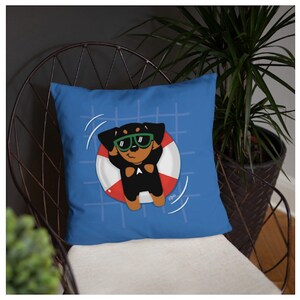 May include: A blue throw pillow with a cartoon image of a dog wearing sunglasses and floating in a red and white life preserver. The dog is black with brown ears and a white patch on its chest.