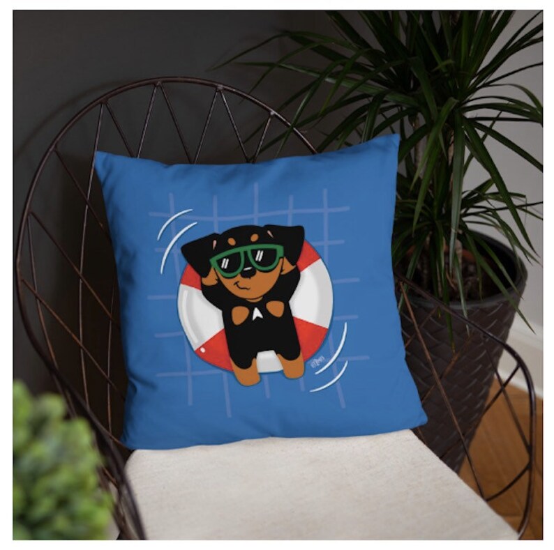 May include: A blue throw pillow with a cartoon image of a dog wearing sunglasses and floating in a red and white life preserver. The dog is black with brown ears and a white patch on its chest.