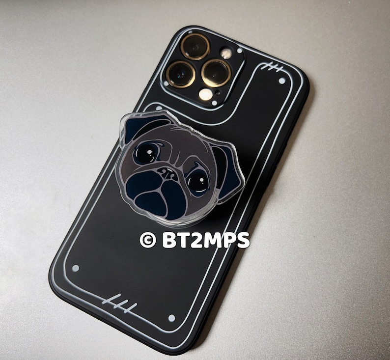 May include: Black phone case with a clear plastic pug phone grip. The phone case has a black camera bump with gold accents. The text "BT2MPS" is printed on the case.