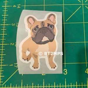 May include: A sticker featuring a cartoon illustration of a French Bulldog. The dog is brown and white with a black nose and big brown eyes. The sticker has the text "&copy; BT2MPS" at the bottom.