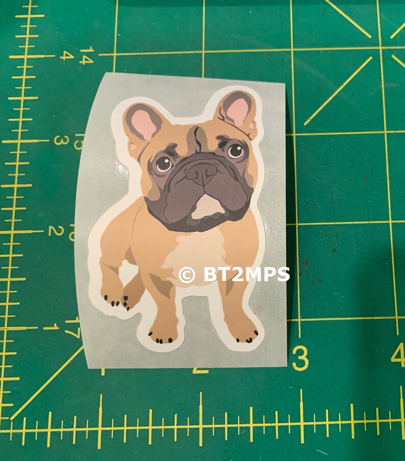 May include: A sticker featuring a cartoon illustration of a French Bulldog. The dog is brown and white with a black nose and big brown eyes. The sticker has the text "&copy; BT2MPS" at the bottom.