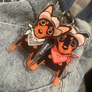 Op de afbeelding: Twee cartoonhonden die cowboyhoeden en bandana's dragen. De honden zijn bruin en zwart met witte accenten. De honden houden een zwarte en zilveren ketting vast. De afbeelding heeft het copyright-symbool en de tekst "BT2MPS".