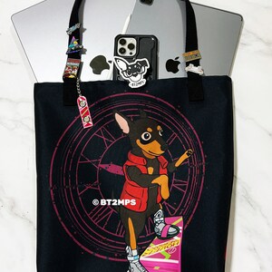 May include: Black tote bag featuring a cartoon dog on a hoverboard, with a red jacket and a clock design. The bag has black handles and is filled with a laptop, tablet, and a phone. The bag is decorated with pins.