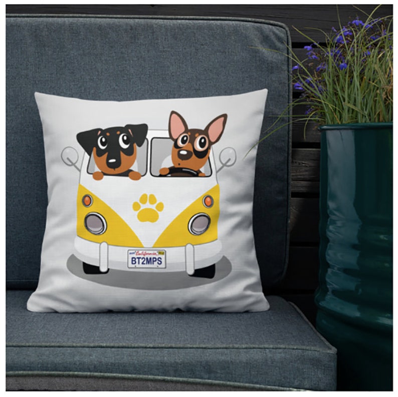 May include: White throw pillow with a cartoon image of two dogs driving a yellow and white vintage van. The van has a paw print on the side and a California license plate that reads "BT2MPS".