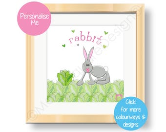 May include: A framed print with a cute cartoon rabbit in a field of green cabbage. The print says "rabbit" in pink letters and has a pink heart above the word. The frame is light wood.
