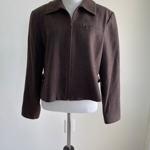 May include: A brown zip-up jacket with a collared neckline. The jacket has a zipper closure and two pockets on the front.