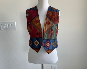 May include: A sleeveless vest with a geometric pattern in shades of red, blue, green, and brown. The vest has a pointed collar and a V-neck.